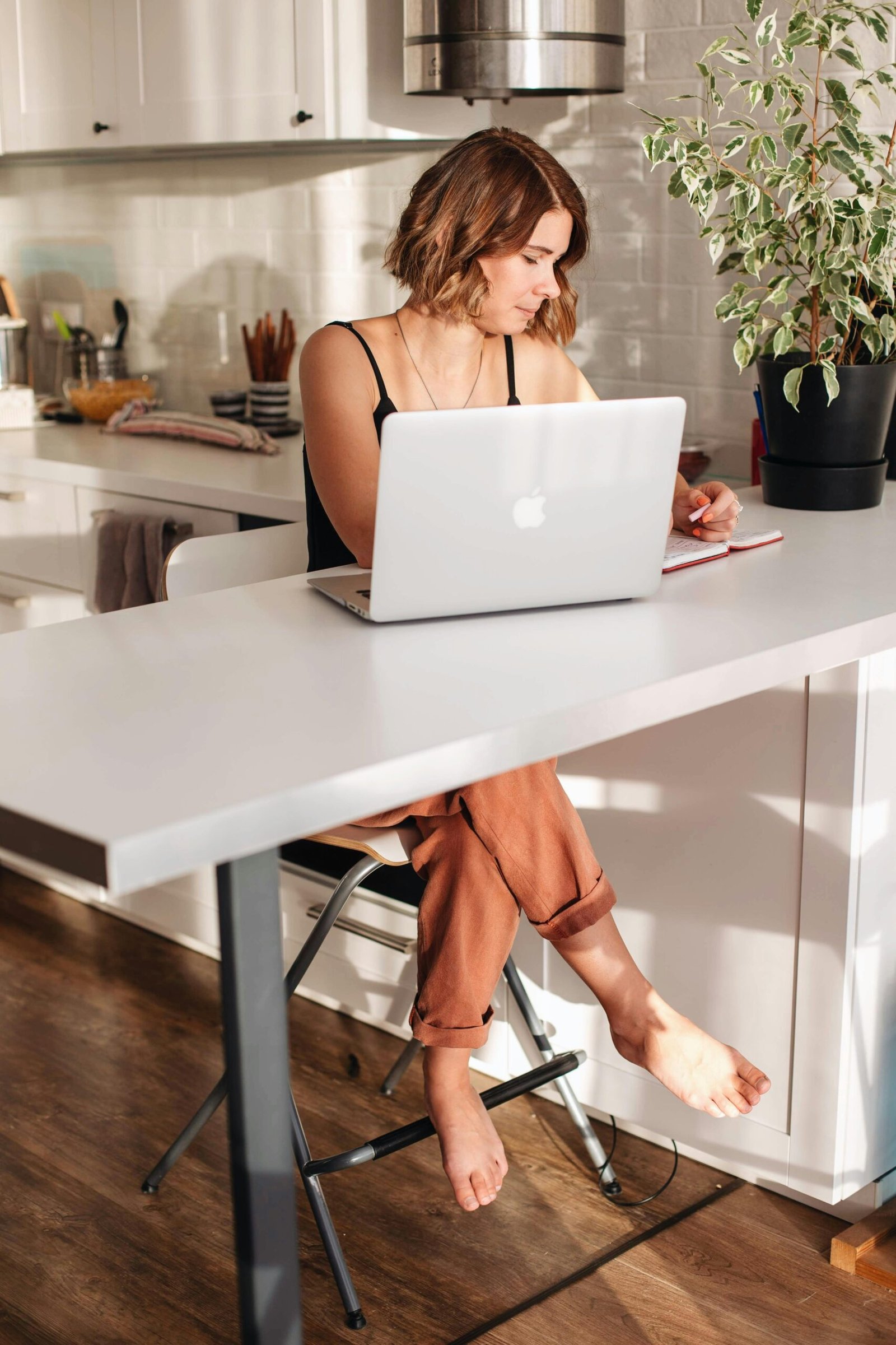 A young woman uses a laptop at a kitchen table for remote work. Bright and airy atmosphere.