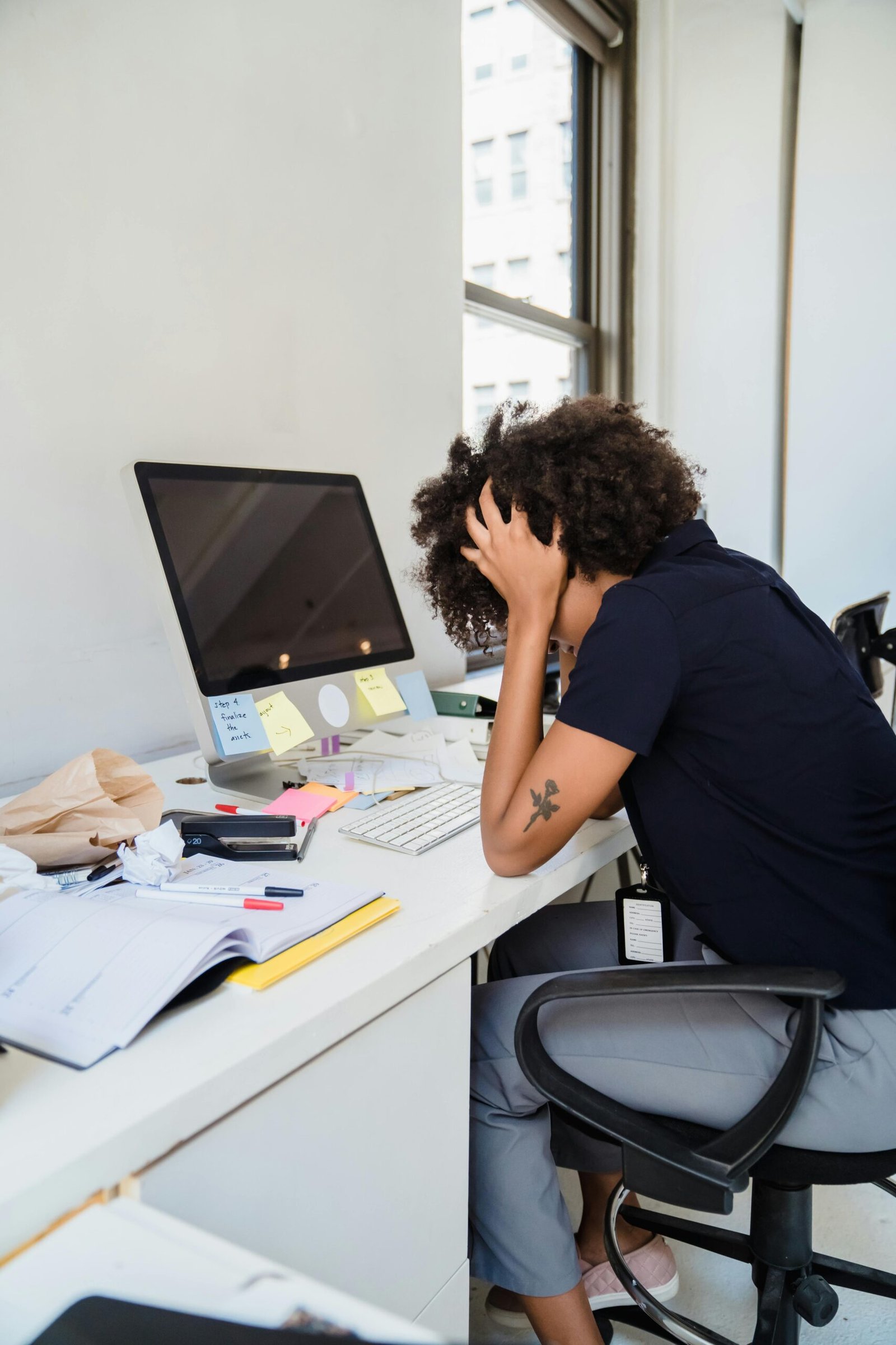 Frustrated woman holding her head at an office desk, overwhelmed by work.