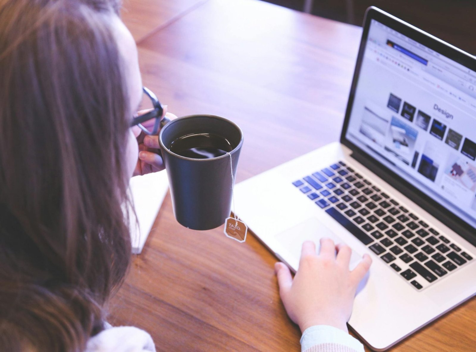 A woman enjoys coffee while browsing the web on a laptop at a home office desk.